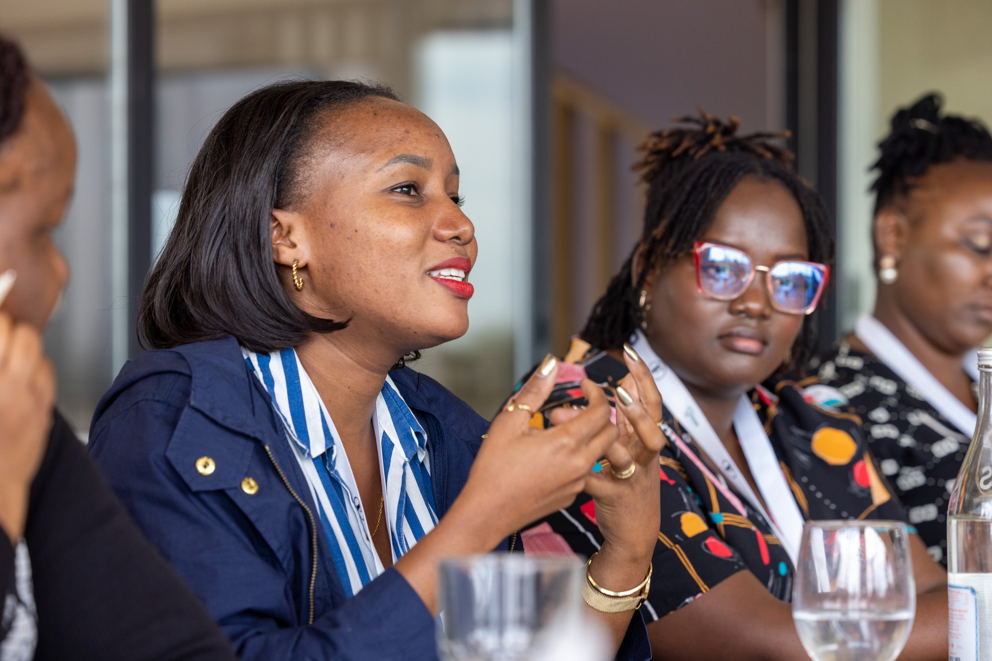 Two women sit next to each other with the one at the forefront speaking to the wider group