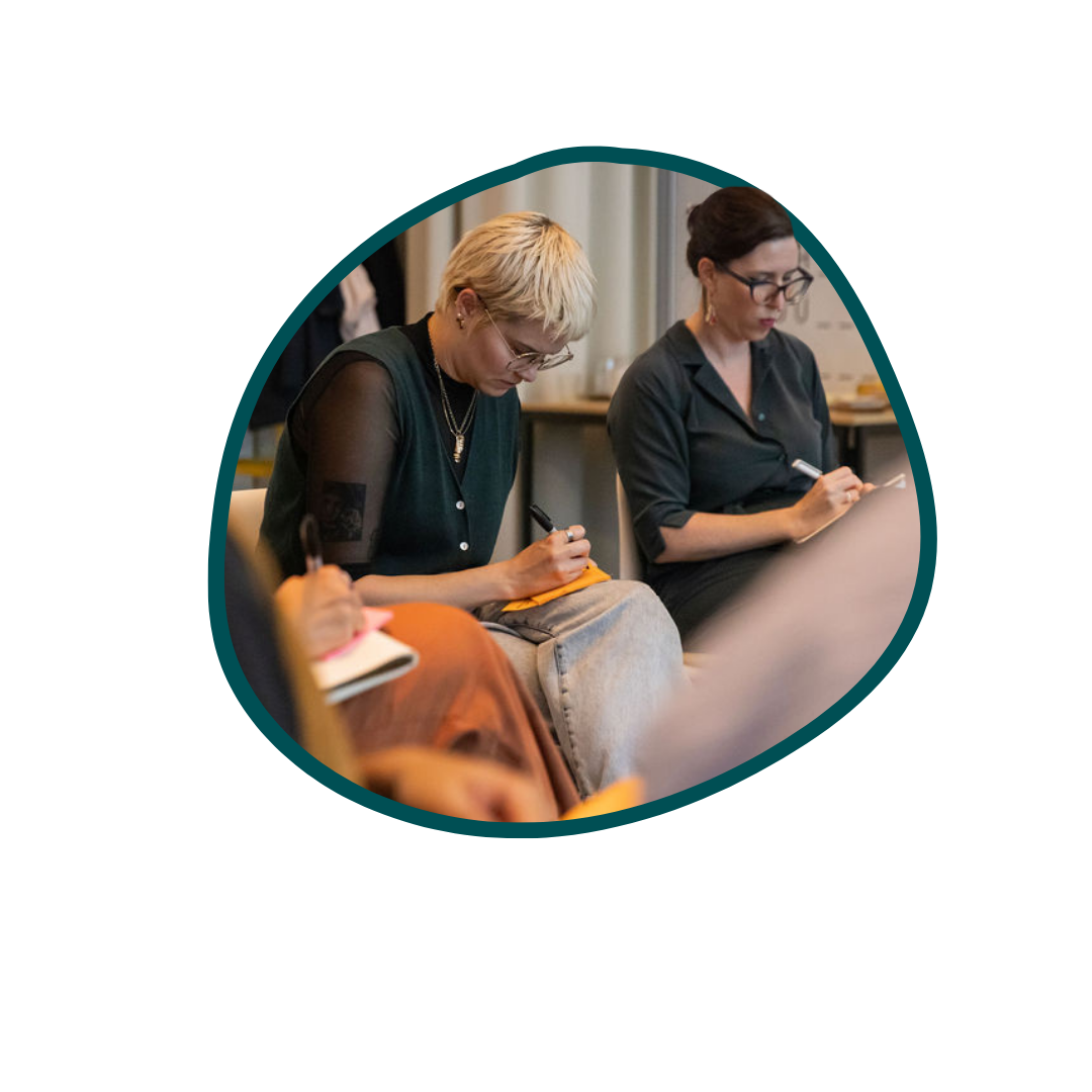 Two women sit next to each other writing in their notebooks