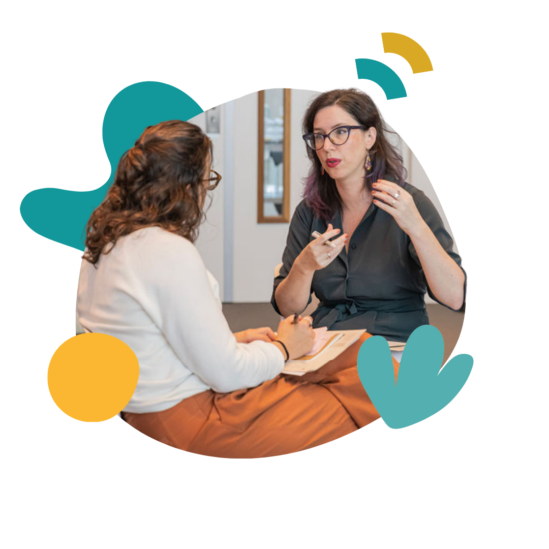 Two women sit together talking and taking notes
