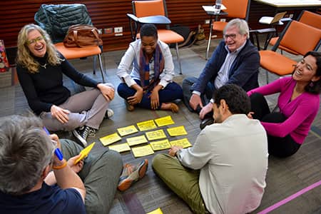 Group of people sitting on the floor, in the center you can see some yellow cards, many smiles and integration