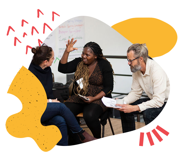 Two women and a man sit on chairs in a group together talking during a Reimagining Collaboration training