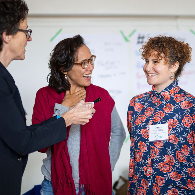 Spring founder Ellen Sprenger holds up a fake microphone to two smiling women during a training