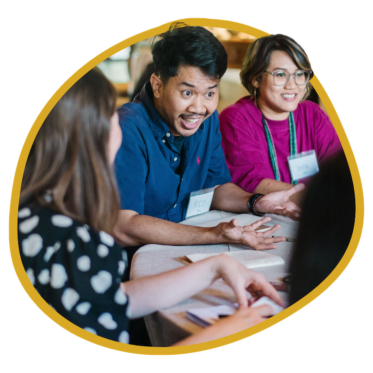 3 people sit together in a group circle with a man in the middle talking expressively