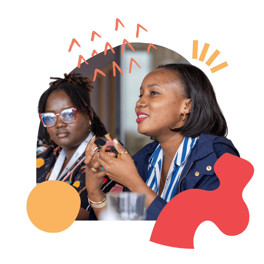 Two women sit next to each other with the one at the forefront speaking to the wider group