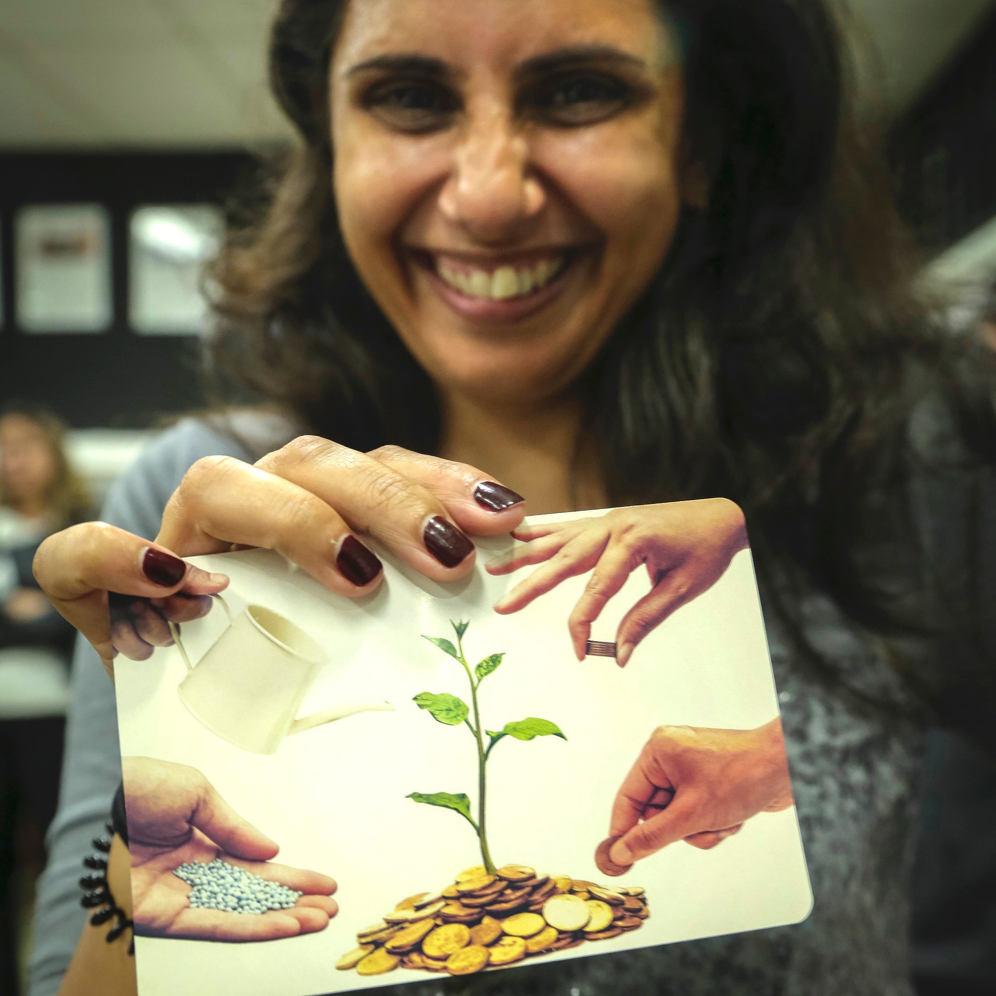 A woman holds a card with the image of a seedling growing out of a pile of coins
