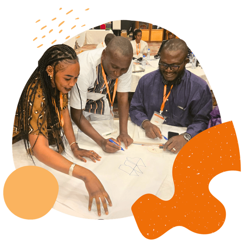 3 people sit around a table during a FIRE training in Brazzaville, smiling and writing on a piece of paper
