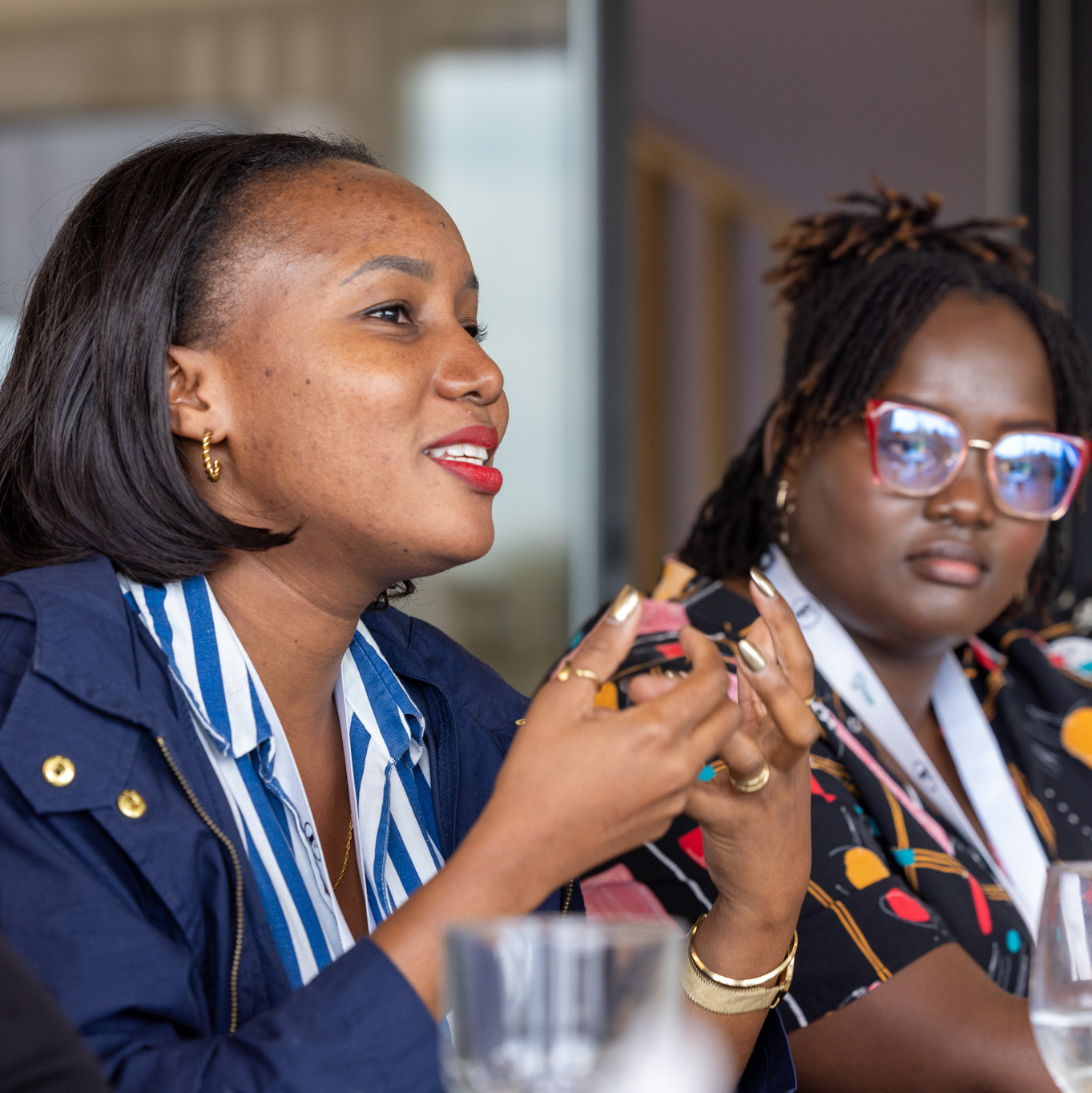 A woman speaks with her hands to a group while another woman sitting next to her listens