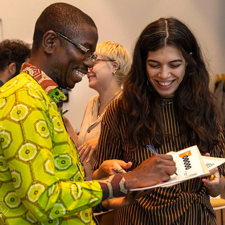 2 people stand next to each other during a training smiling as they write on a piece of paper